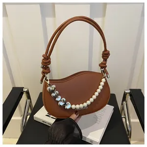 Detail of a brown shoulder bag with a silver heart and pearl chain and fashion text