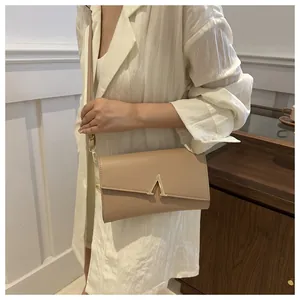 Détail du sac bandoulière en cuir beige avec boucle dorée en V porté par un modèle