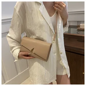 Détail du sac beige avec fermoir en V doré et fine bandoulière sur veste blanche