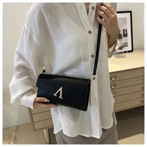 Détail d'un sac bandoulière en cuir noir avec boucle dorée en V sur une chemise en lin blanc