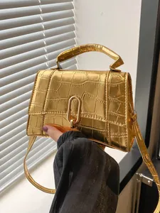 Detail of gold crocodile embossed hourglass handbag with metallic clasp and adjustable strap