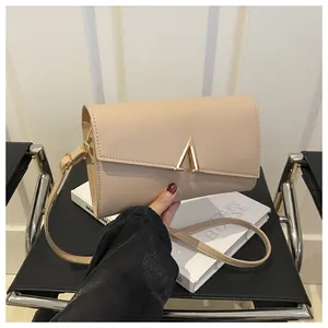 Détail d'un sac enveloppe en cuir beige avec fermoir en métal doré en V sur le rabat