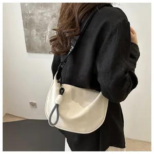 Détail du sac demi-lune crème avec large bandoulière noire et nœud porté par le modèle