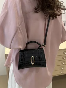 Detail of black croc-effect mini square bag with gold U-shaped lock on a model