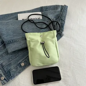 Lichtgroene nylon telefoontas met trekkoord en zwarte riem op een denim achtergrond