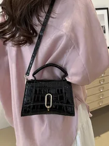 Close-up of black crocodile pattern handbag with gold U-shaped metal lock on model