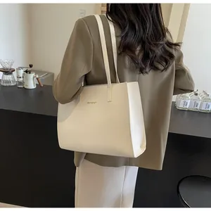 Détail du sac cabas beige minimaliste avec logo doré à l'épaule dans un café