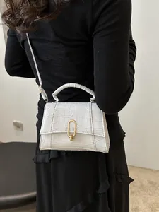 Detail view of a white croc-embossed small square bag with elegant gold metal clasp