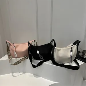 Trois sacs à bandoulière en toile en forme de croissant rose, noir et blanc sur un socle