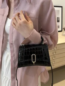Detail of black glossy faux-crocodile leather handbag with golden metal buckle