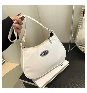 Close-up of white nylon crescent shoulder bag featuring black oval logo and silver zipper