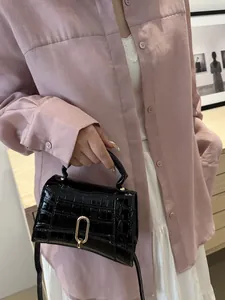 Detail of black crocodile-embossed mini handbag with gold metal hardware and curved base