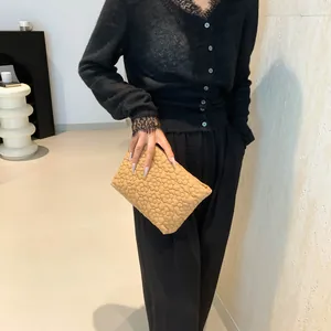 Beige bubble texture clutch bag with 3D quilted floral embroidery held by model