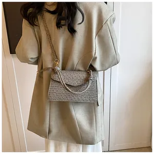 Chic grey crocodile pattern handbag with gold hardware and spiral handle on green blazer