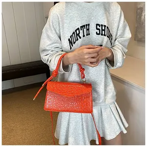 Close-up of bright orange crossbody bag with crocodile texture and gold hardware