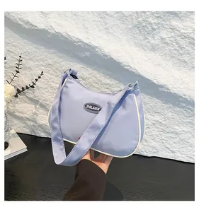 Detail of light blue nylon crescent bag showing the logo patch and white piping trim