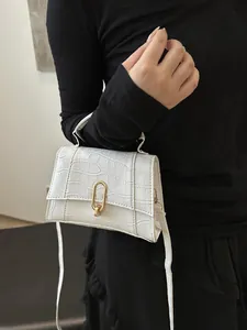 Detail of white crocodile pattern crossbody bag with golden lock held by a model