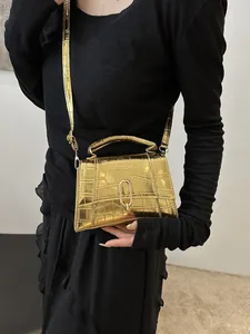 Detail of gold crocodile embossed mini handbag featuring a U-shaped metallic lock and top handle