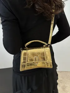 Detail of metallic gold crocodile-embossed mini bag with unique curved base and metal lock