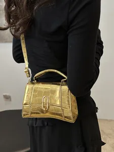 Detail of gold crocodile embossed leather handbag with curved base and metallic hardware