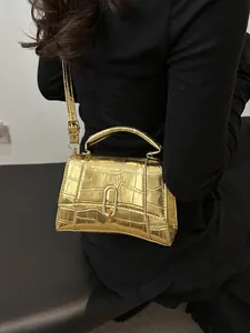 Detail of gold crocodile embossed mini handbag featuring a curved base and metal ring