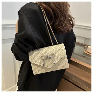 Détail du sac à bandoulière tissé crème avec boucle papillon en strass et chaînes dorées