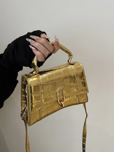 Detail of gold crocodile embossed handbag with metallic U-shaped lock and glossy finish
