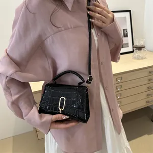 Elegant black crocodile embossed crossbody bag with gold buckle on a pink shirt model