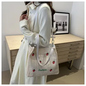 Détail du sac cabas tissé avec broderie fraise et bandoulière en cuir élégante