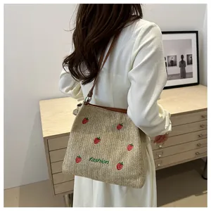 Détail du sac seau tressé avec broderie fraise et bandoulière en cuir marron