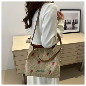 Détail de la broderie fraise sur un sac cabas en paille avec bandoulière en cuir brun