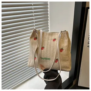 Détail du sac cabas en paille avec broderie fraise et bandoulières en cuir blanc