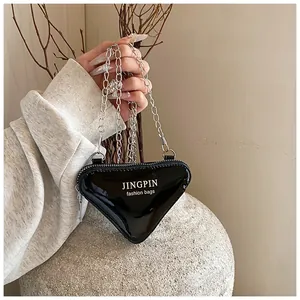 Makroaufnahme einer schwarzen dreieckigen Ledertasche mit Silberkette und Markenaufdruck