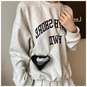 Schicke schwarze glänzende Mini-Dreieckstasche mit Silberkette an der Schulter des Models
