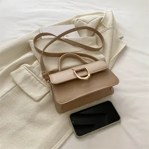 Mini beige leather handbag with gold D-buckle and shoulder strap on cream blazer