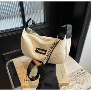 Détail du sac croissant blanc texturé avec bandoulière large à logo et étiquette