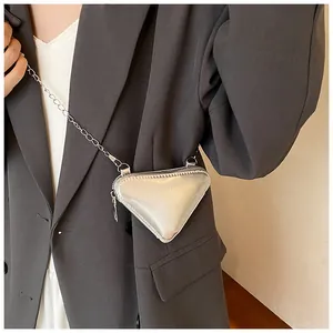 Detail einer silbernen Dreieck-Minitasche mit Kette über einem grauen Blazer