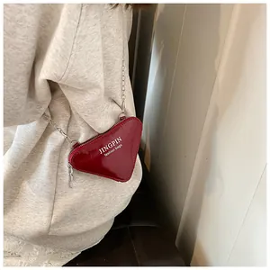 Detail der roten herzförmigen Lackleder-Umhängetasche an einem Modell mit Kettenriemen