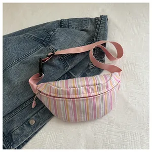 Dettaglio borsa pettorale in nylon a righe colorate con tracolla rosa regolabile su denim