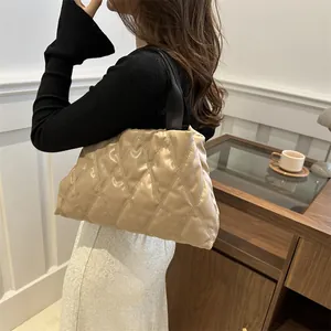 Detail of beige quilted puffer handbag with black straps in a minimalist indoor setting