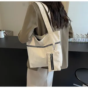 Detail of a large white tote bag with black zippers and matching small pouch on a model