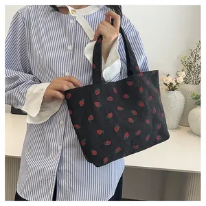 Détail du sac cabas en velours côtelé noir avec motif fraise rouge à la main