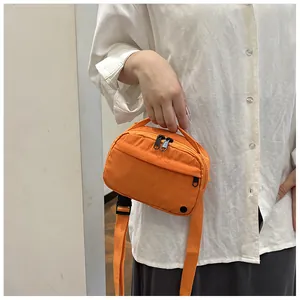 Detail of a bright orange nylon crossbody bag with dual zippers and adjustable strap