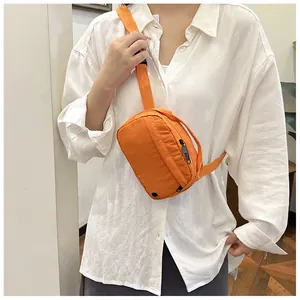 Orange mini crossbody bag worn as a chest pack over a white shirt, detail view