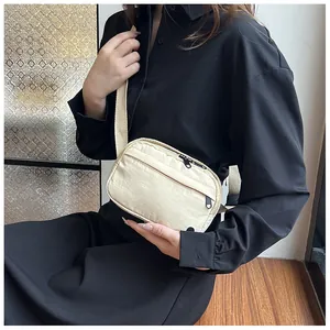 Close-up of cream nylon crossbody bag showing multiple pockets and adjustable strap