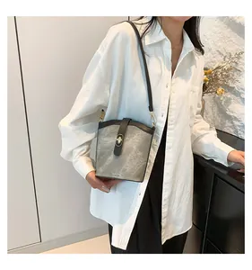 Detail of grey bucket bag with contrast trim and metal turn-lock on a shoulder strap
