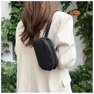 Detailed view of the black nylon crossbody bag worn over a beige blazer in a sunny garden