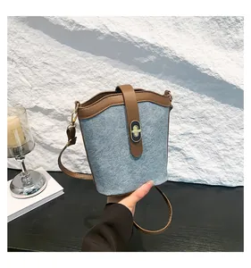 Detail of blue denim bucket bag with brown leather trim and oval metal twist lock