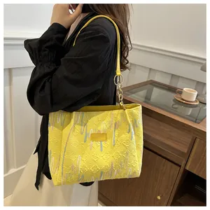 Detalle del bolso tote amarillo de PU con costuras onduladas y correa de cadena dorada