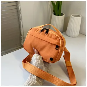 Close-up of vibrant orange nylon crossbody bag with dual zippers and adjustable strap